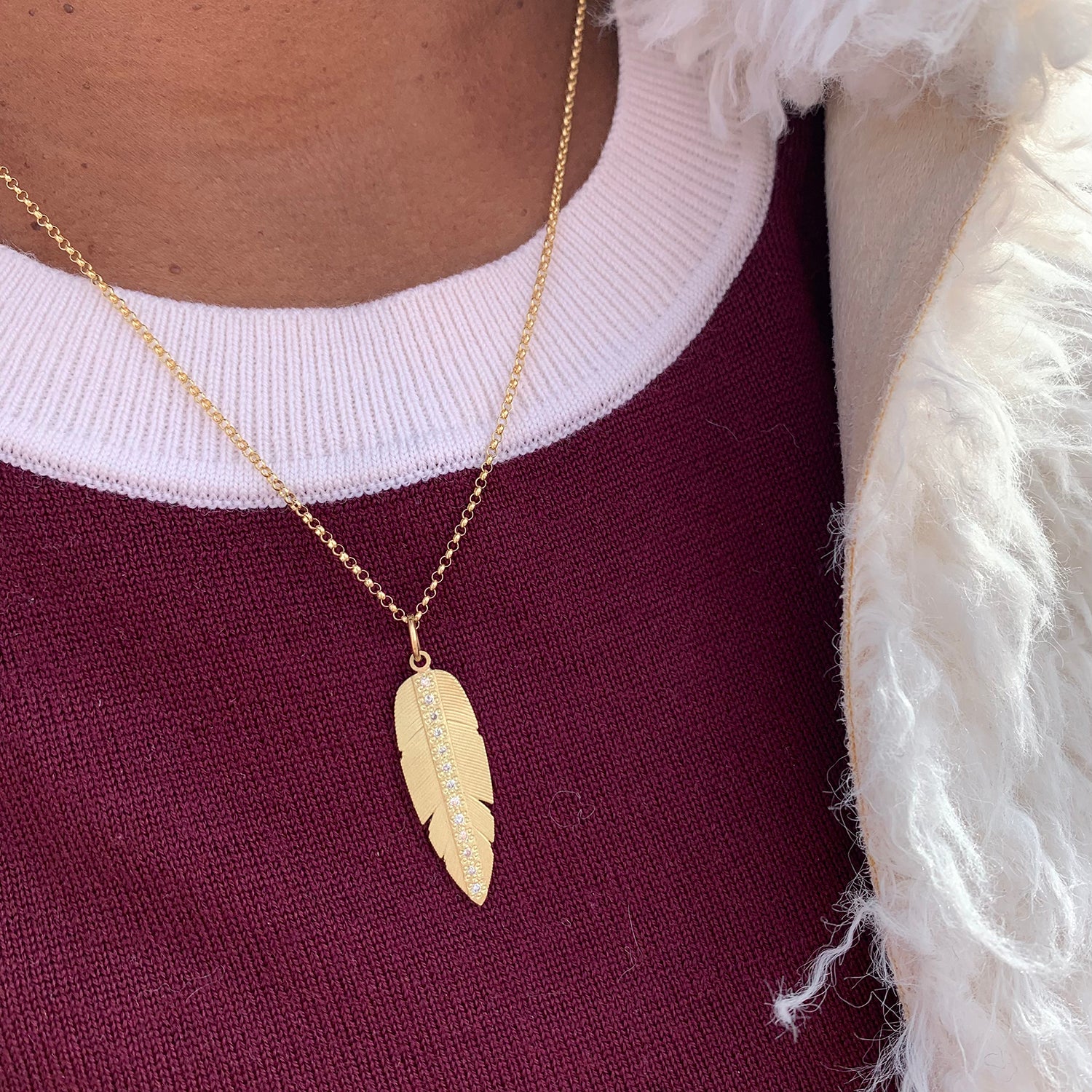 Large Gold & Diamond Slender Feather Charm on African American female model in red sweater | Rebecca Myers Collection