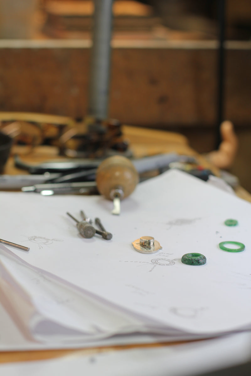 Jewelry design sketches with wax models, a metal component, and tools on the studio workbench